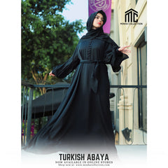 Woman wearing a black Turkish abaya on a balcony with a Minha Collection logo.
